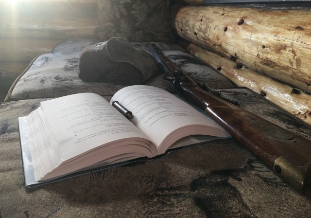 A book lies open next to a muzzleloader with wooden stock